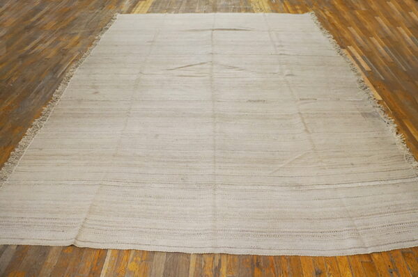 Neutral flatweave rug featuring faint horizontal light brown stripes displayed on distressed hardwood flooring.