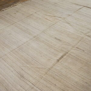 Natural toned flatweave rug featuring visible seams and striations on a brown wood floor.