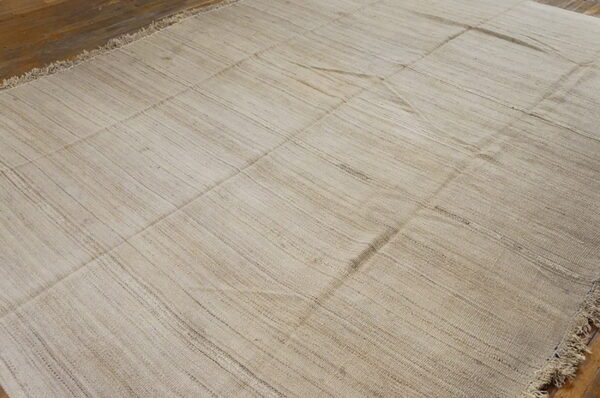 Natural toned flatweave rug featuring visible seams and striations on a brown wood floor.