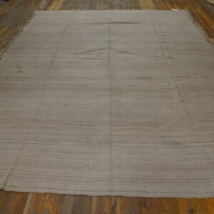 Taupe flatweave rug featuring subtle horizontal striping and short fringe on wood plank flooring.