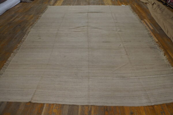 Taupe flatweave rug featuring subtle horizontal striping and short fringe on wood plank flooring.