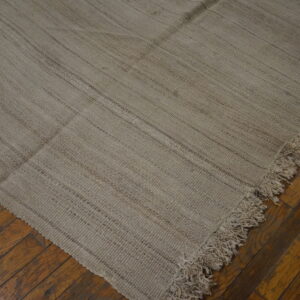 Flat-woven beige rug with visible dark striping and long fringe lies on distressed wood flooring.