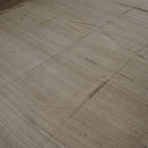 Textured tan flatweave rug featuring visible vertical striations and stitched seams over dark wood planks.