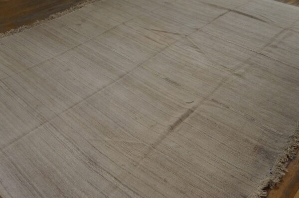Textured tan flatweave rug featuring visible vertical striations and stitched seams over dark wood planks.