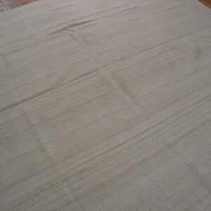 Light natural-colored flatweave rug with horizontal seams displayed over glossy brown wood flooring.