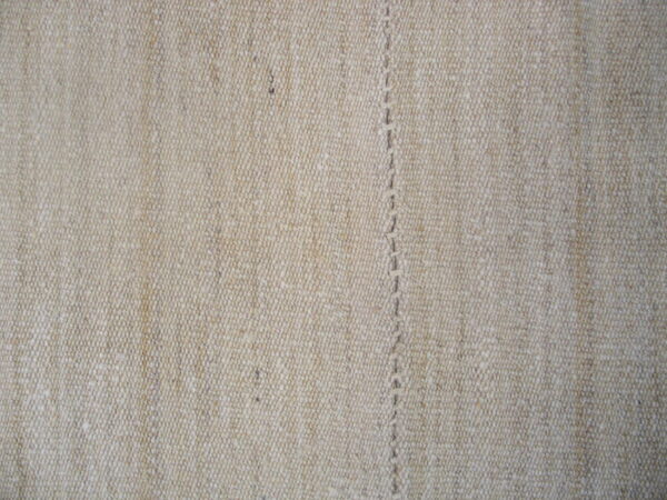 Detailed view of a heathered oatmeal flatweave texture with a central vertical stitched seam.
