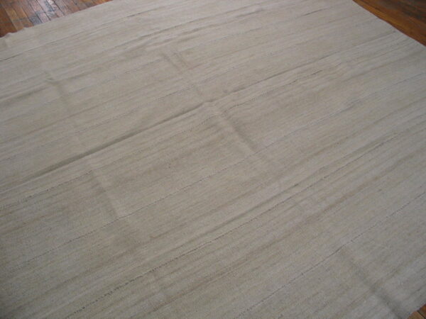 Natural beige flatwoven rug with stitched horizontal lines covering a dark wood floor.