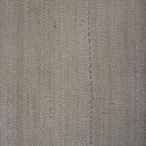 Tightly woven, textured beige rug surface featuring a visible vertical seam of thick, hand-stitched thread.