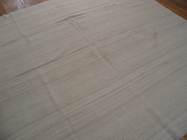 A large, textured flatweave rug in a natural beige color lies on dark wood floors.