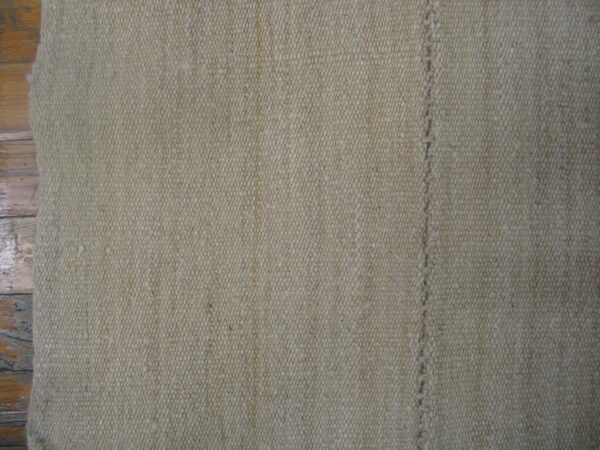 Close-up of a textured natural beige rug showing a vertical stitched seam on a wooden floor.