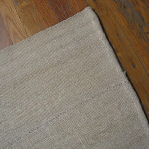 Beige textured rug showing stitched seams rests on dark amber wooden plank flooring.