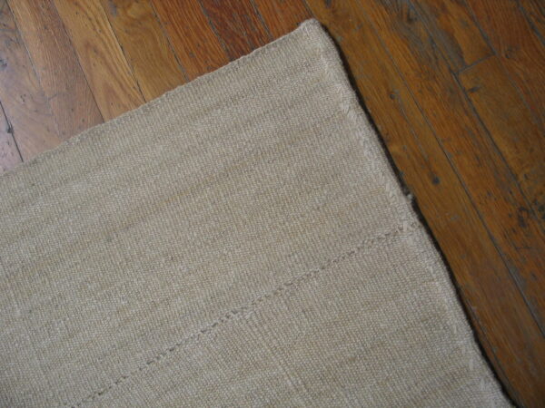 Beige textured rug showing stitched seams rests on dark amber wooden plank flooring.