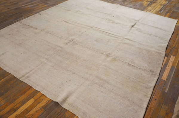 Light neutral-toned flatweave rug featuring stitched panels on rustic wood flooring.