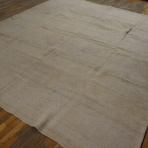 Beige flatwoven rug with visible stitched panels covers dark distressed wood flooring.