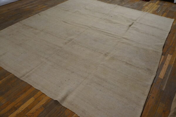 Beige flatwoven rug with visible stitched panels covers dark distressed wood flooring.