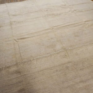 A large, off-white flatweave rug with stitched horizontal panels covers rustic wood flooring.