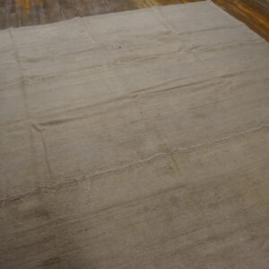 Neutral tan flatweave rug featuring visible stitched panels covers dark plank flooring.
