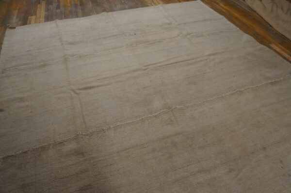 Neutral tan flatweave rug featuring visible stitched panels covers dark plank flooring.