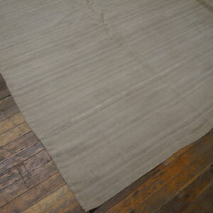 A light gray flatweave rug with subtle horizontal bands rests on distressed, dark brown wood floors.