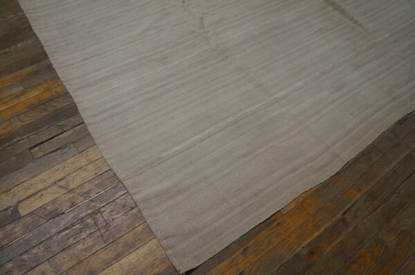 A light gray flatweave rug with subtle horizontal bands rests on distressed, dark brown wood floors.
