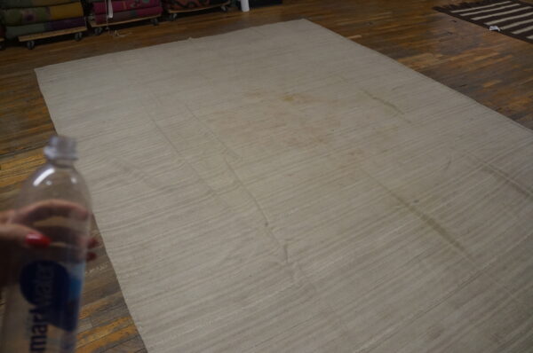 The flatwoven light beige rug with visible seams lies on dark hardwood flooring.