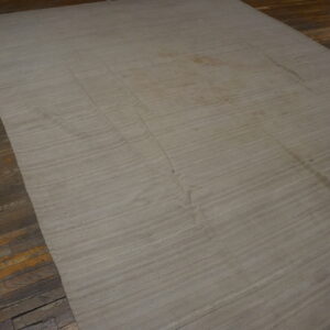 Large natural-colored flatweave rug with horizontal seams rests on worn hardwood planks.