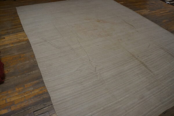 Large natural-colored flatweave rug with horizontal seams rests on worn hardwood planks.