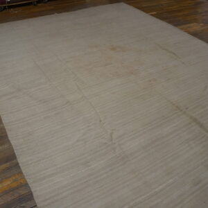 Natural toned flatweave rug with subtle horizontal lines displayed on dark wooden floorboards.