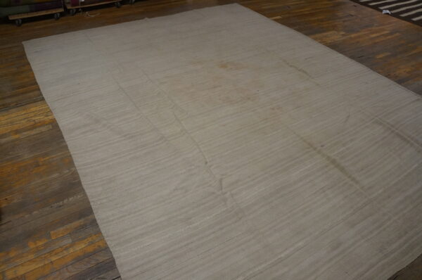 Natural toned flatweave rug with subtle horizontal lines displayed on dark wooden floorboards.