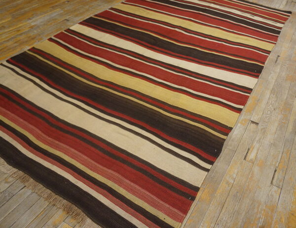 A flat-woven striped rug with red, brown, cream, and yellow bands rests on weathered wood flooring.