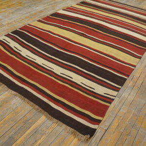 A flat-woven rug with red, gold, cream, and brown horizontal stripes lays on distressed wooden flooring.