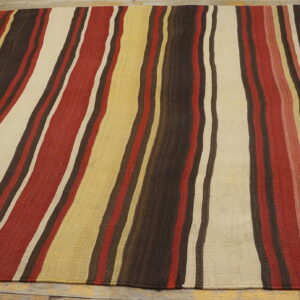 Flatweave rug with thick vertical stripes in dark brown, red, cream, and yellow resting on wood floors.