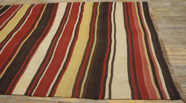 Flatweave rug with thick vertical stripes in dark brown, red, cream, and yellow resting on wood floors.
