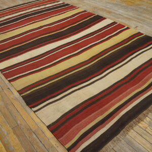 Flatweave rug with lengthwise stripes of deep red, brown, cream, and yellow on old wood flooring.