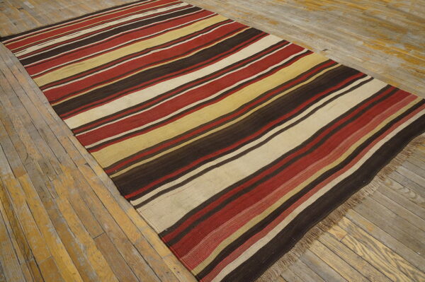 Flatweave rug with lengthwise stripes of deep red, brown, cream, and yellow on old wood flooring.