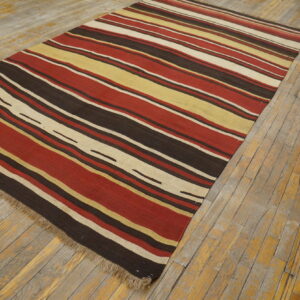 Red, brown, yellow, and cream striped flatweave rug displayed on rustic wooden plank flooring.