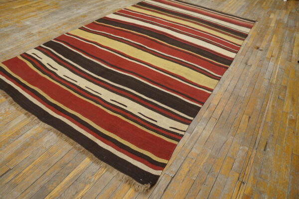 Red, brown, yellow, and cream striped flatweave rug displayed on rustic wooden plank flooring.