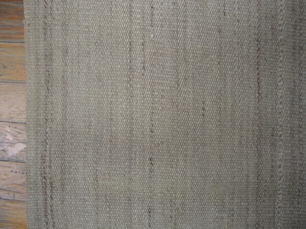 Muted beige, tightly woven low-profile rug with vertical texture rests on warm hardwood planks.