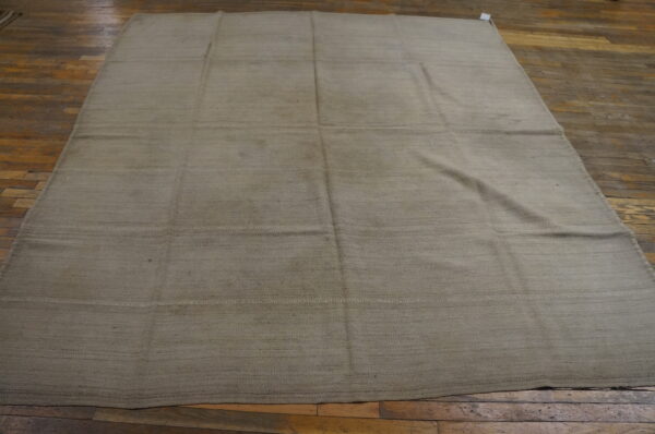 A large, solid beige flatweave rug with horizontal seams rests on rustic brown plank wood flooring.