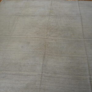 Neutral taupe flatweave rug featuring faint horizontal stripes, displayed on dark wood planks.