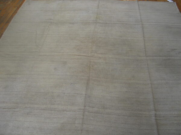Neutral taupe flatweave rug featuring faint horizontal stripes, displayed on dark wood planks.