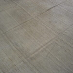 A light gray, low-pile rug with visible seams separating ribbed, rectangular panels on a wood floor.