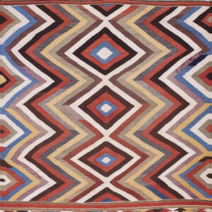 Flatweave rug in red, blue, brown, and cream with bold zigzags forming large central diamonds.