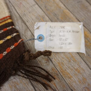 Close-up of a brown, cream, orange, and yellow flatweave textile with fringe resting on weathered wood.