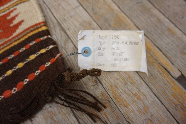 Close-up of a brown, cream, orange, and yellow flatweave textile with fringe resting on weathered wood.