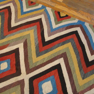 Multi-colored geometric rug featuring concentric zigzags and diamonds on a warm wood floor.