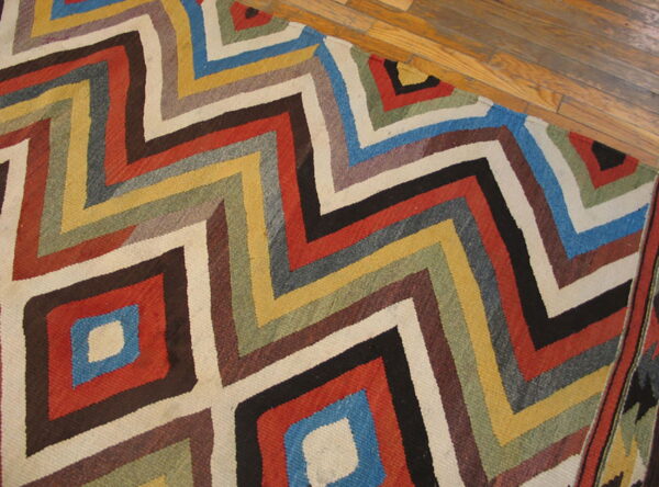 Multi-colored geometric rug featuring concentric zigzags and diamonds on a warm wood floor.