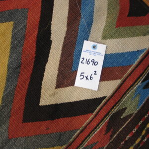 Flatwoven rug detail showing bold stepped geometric patterns in rust, green, yellow, blue, and tan.