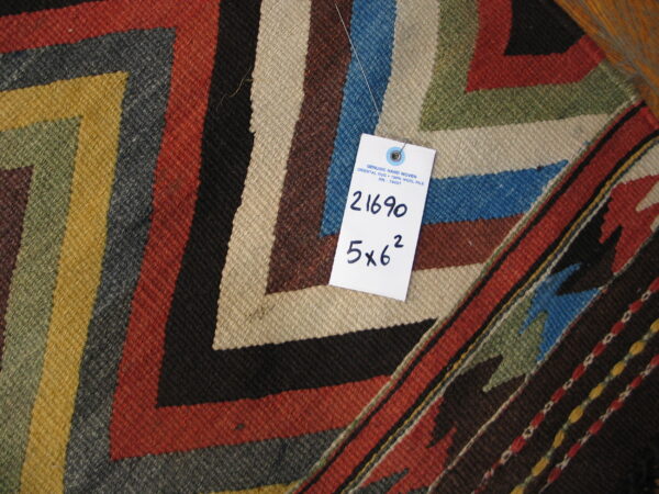 Flatwoven rug detail showing bold stepped geometric patterns in rust, green, yellow, blue, and tan.