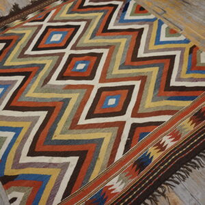 Colorful flatwoven rug featuring complex diamond and zigzag patterns displayed on rustic hardwood flooring.